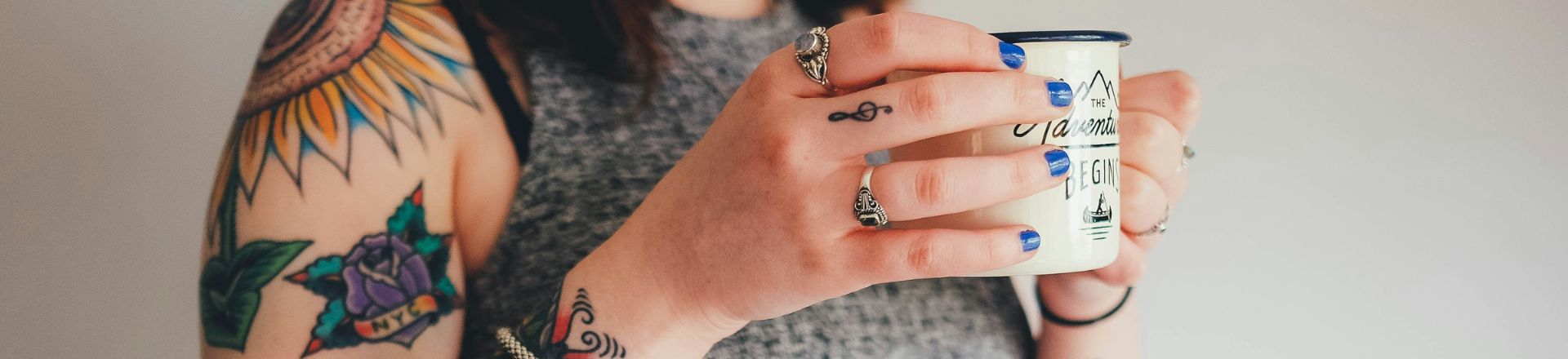 a woman covered with fake tattoo that looks real holding a cup of coffee